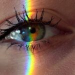 Problem-Solving - Closeup of crop anonymous sad female with green eyes and rainbow light on face looking at camera