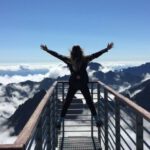 Success - Person Standing on Hand Rails With Arms Wide Open Facing the Mountains and Clouds