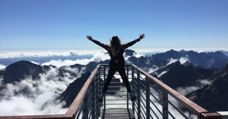 Success - Person Standing on Hand Rails With Arms Wide Open Facing the Mountains and Clouds